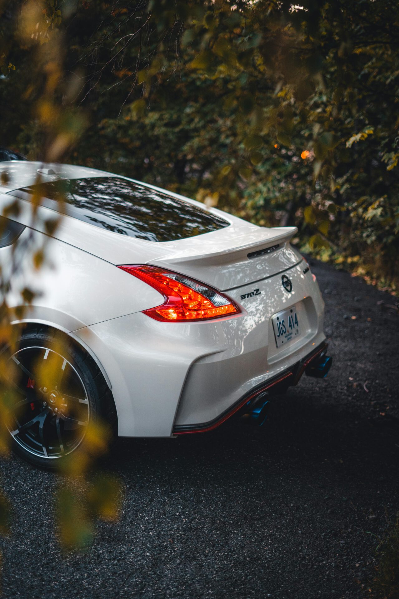 A stylish white Nissan 370Z with vibrant taillights captured in a lush, leafy setting.